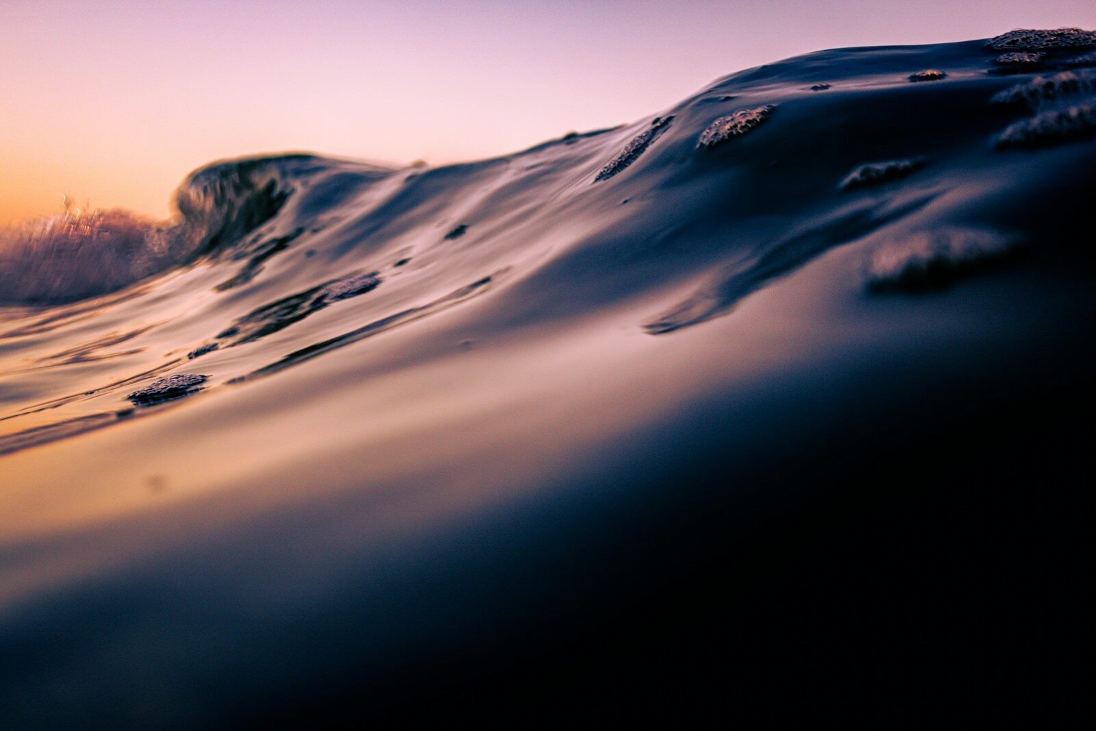 An ocean wave breaking at sunset with vibrant sky colors